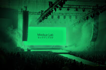 Concert venue with neon green jumbo display screen, fog effects, packed crowd below