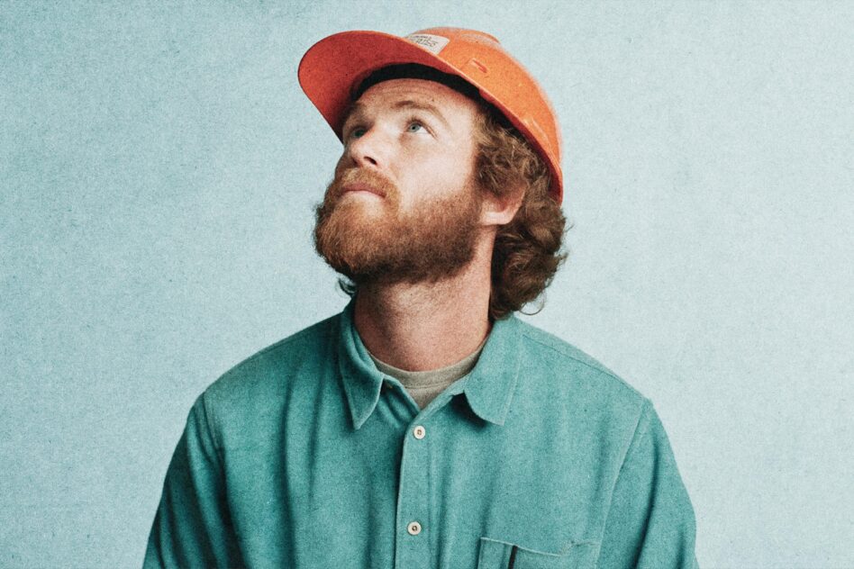 Man in orange hard hat and teal shirt looking upwards. Construction-themed portrait for design assets. Use in graphics or mockups. Rugged style.