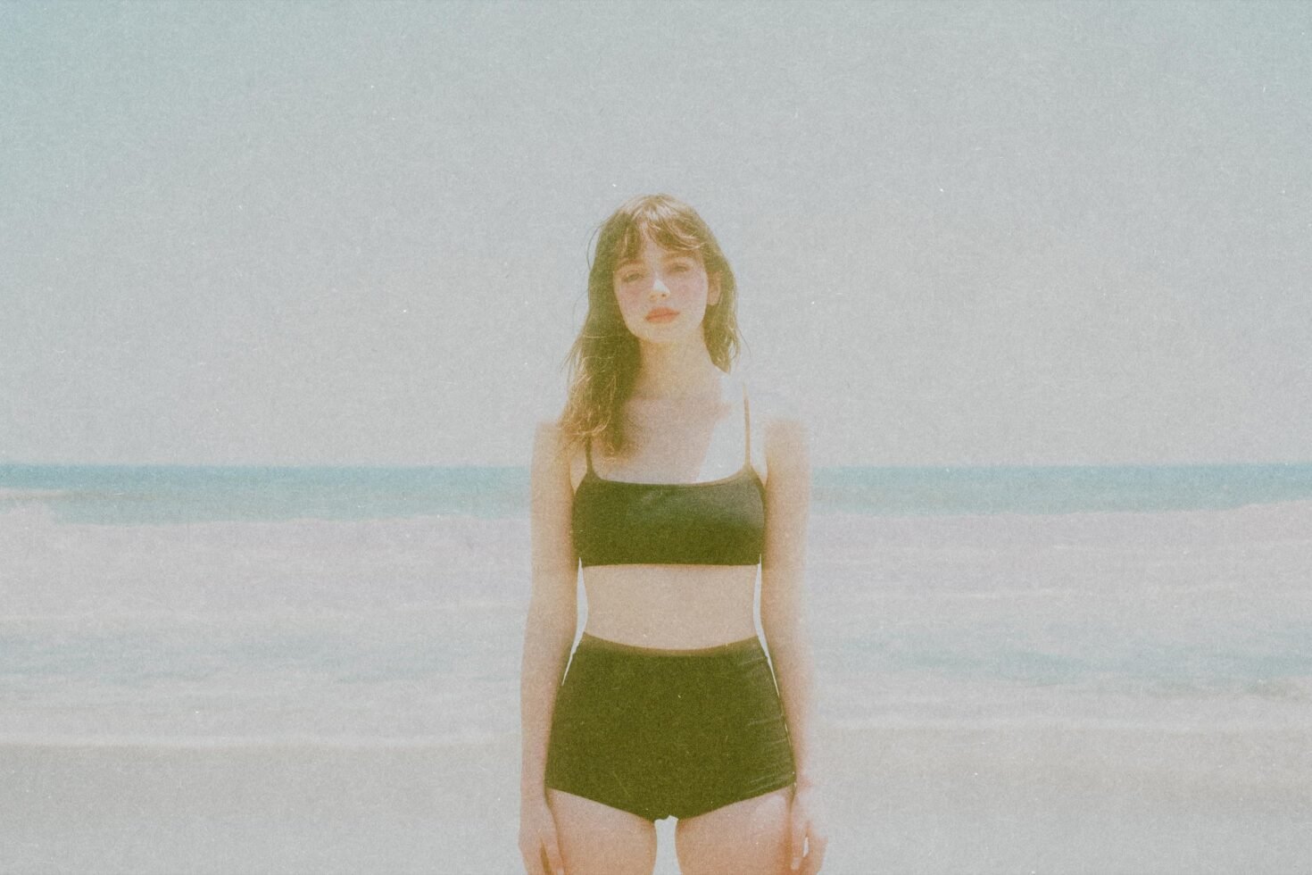 Vintage beach photo featuring a person in retro swimwear standing by the sea with a grainy film effect perfect for design mockups and graphic projects.