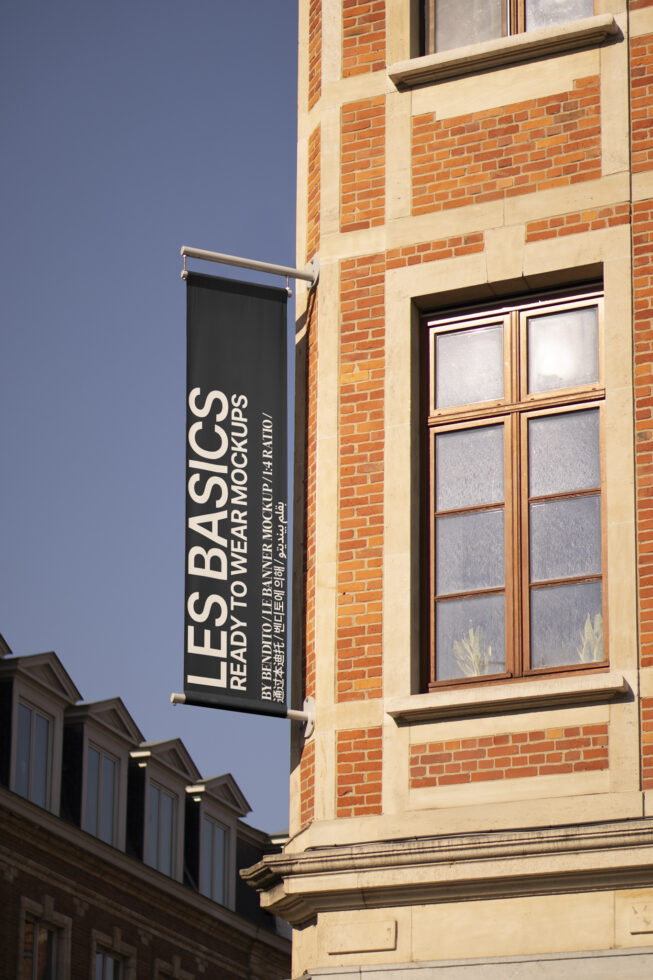 Vertical banner mockup on urban brick building exterior with window. Ideal for showcasing branding designs. Keywords: banner, mockup, building, exterior.