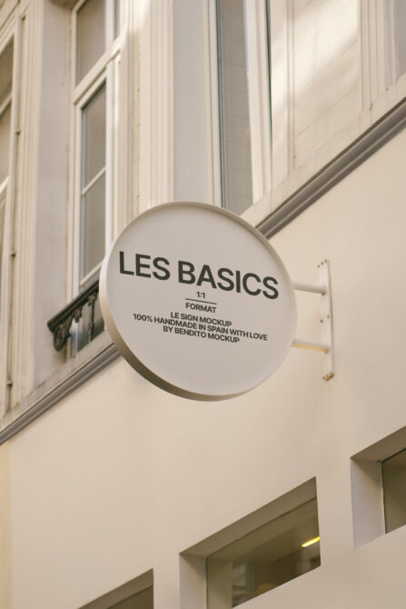 Round cream-colored projecting sign with black text mounted on white facade near classical architectural elements