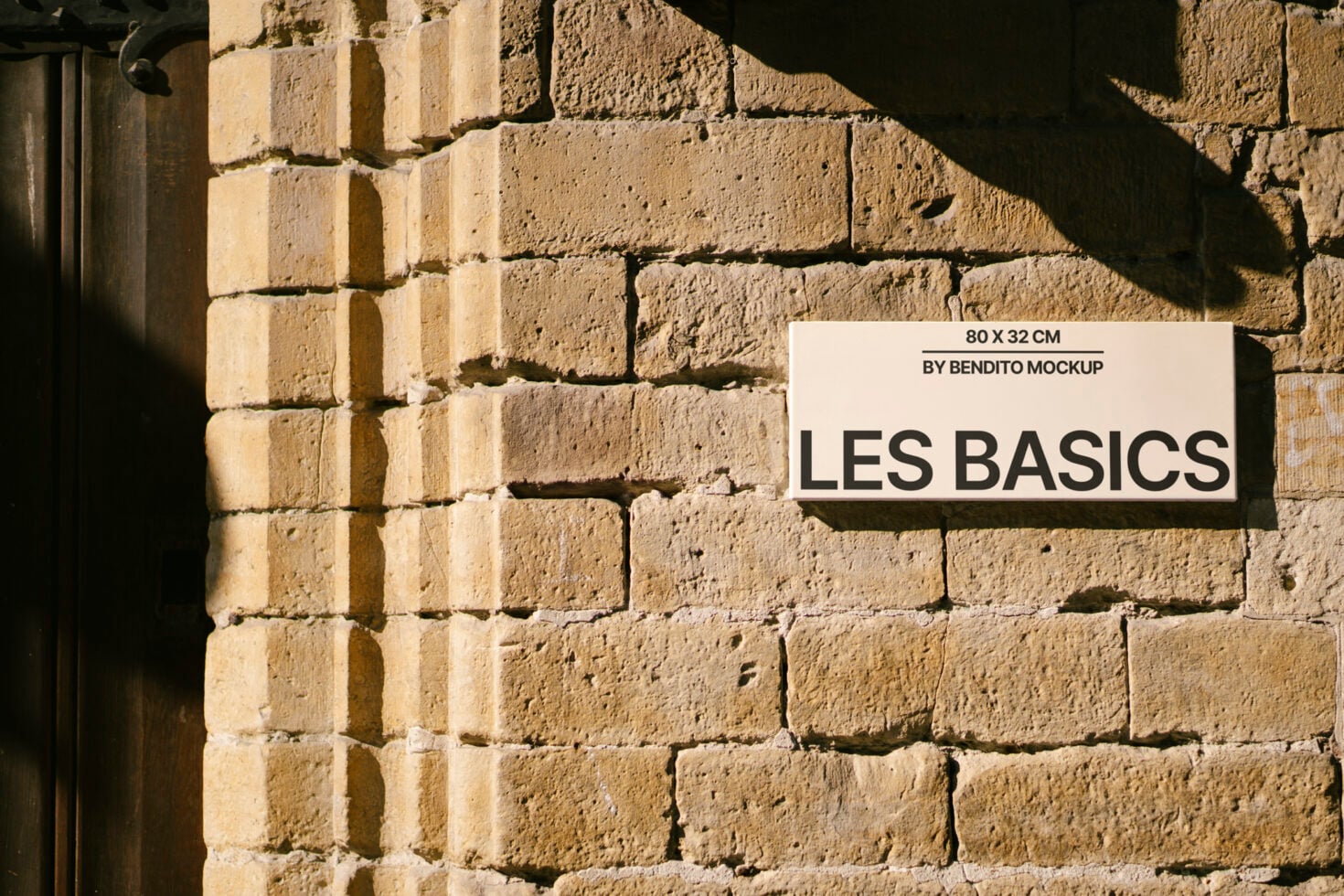 White rectangular sign with black text on rough sandstone brick wall with dramatic sunlight shadows