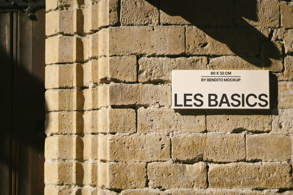 White rectangular sign with black text on rough sandstone brick wall with dramatic sunlight shadows
