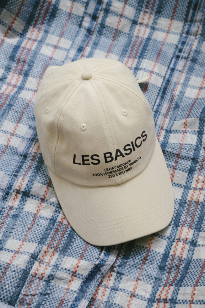 Cream colored cap with Les Basics logo on blue plaid cloth surface