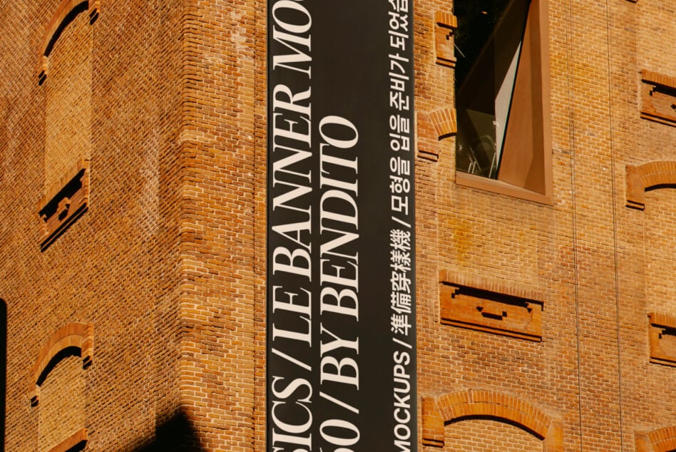 Dark vertical banner on terracotta brick exterior with multilingual text, cast shadow from sunlight