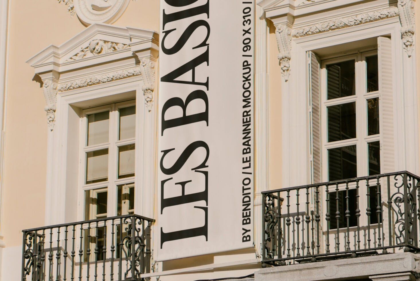 Cream neoclassical facade with ornate columns, vertical banners displaying text, iron railings on balconies