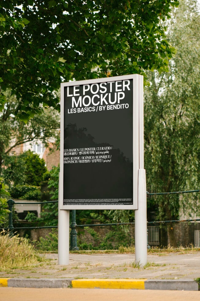Black poster mockup on vertical white pole under dense green tree canopy