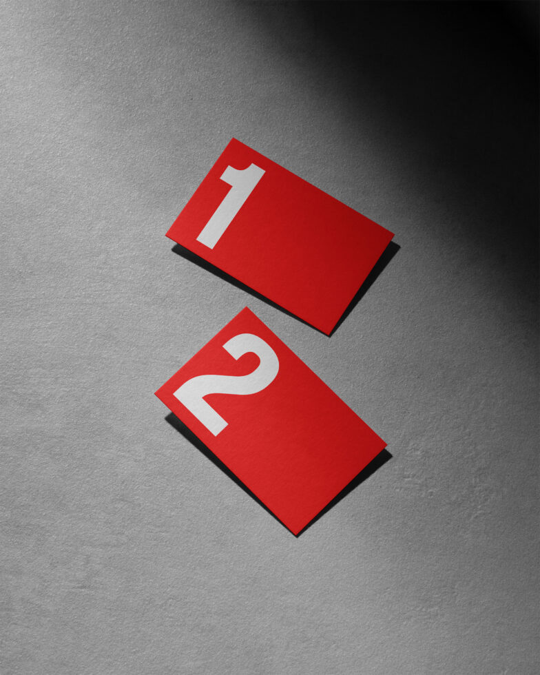 Red paper cards with white numbers 1 and 2 against a textured gray background. Perfect for mockups, print designs, graphic elements, minimalist style.