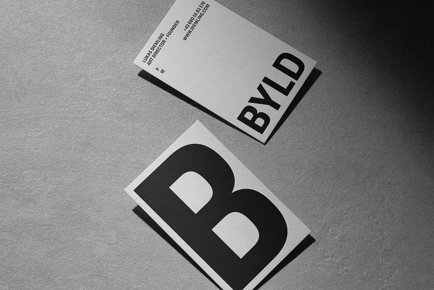 Minimal business card mockup with bold typography featuring the letter B and BYLD text on a textured surface. Ideal for graphic designers seeking modern templates.