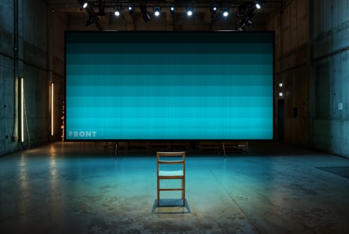 Modern industrial setting with a large screen displaying aqua gradients. A wooden chair sits at the center. Perfect for mockup design presentations.