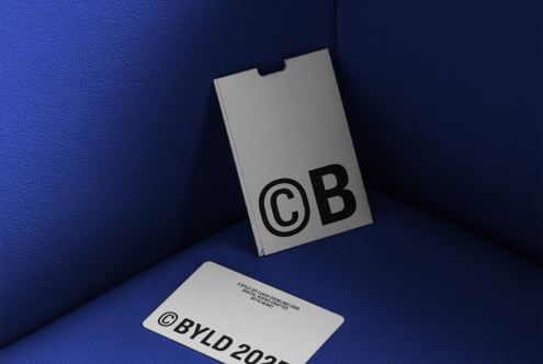 A minimalist mockup displaying a gray card and package with bold black typography on blue leather. Ideal for designers seeking sleek branding assets.