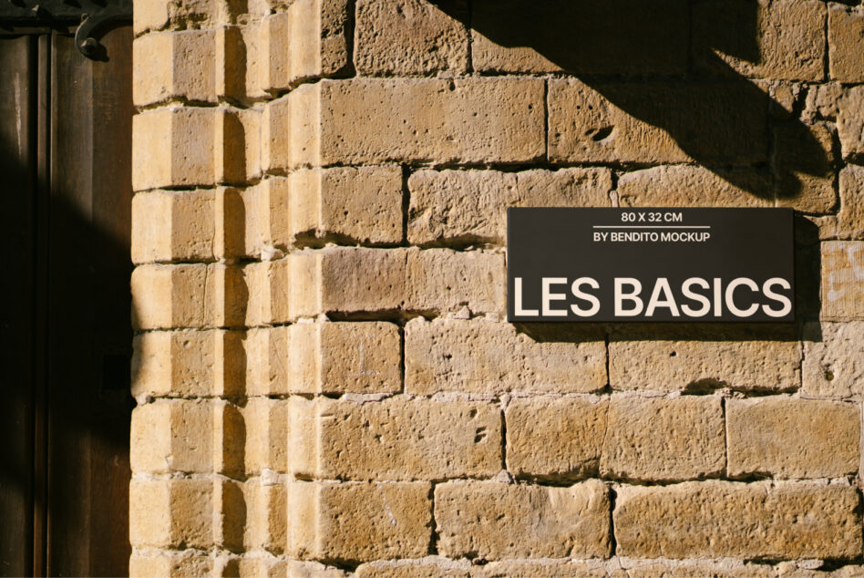 Dark horizontal sign with white text on rough sandstone brick wall with dramatic sunlight shadows