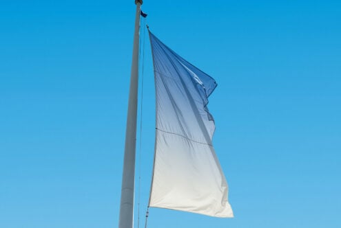 Blue and white flag on flagpole against clear sky. Ideal for flag mockup designs, promotional graphics, or outdoor display templates.