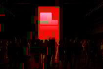 Silhouettes of people stand in front of a large red illuminated screen in a dark room, perfect for technology event graphics, digital art backgrounds.