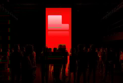 Silhouettes of people stand in front of a large red illuminated screen in a dark room, perfect for technology event graphics, digital art backgrounds.
