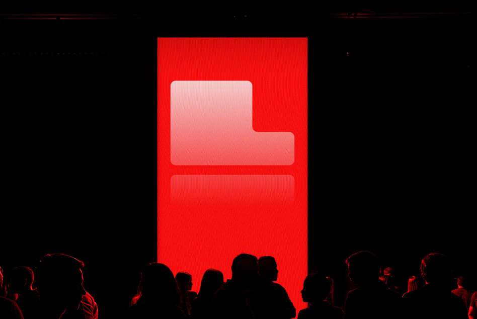 Bold red screen with logo displayed in a dark room full of silhouetted people innovative digital asset mockup for creative designers SEO keywords