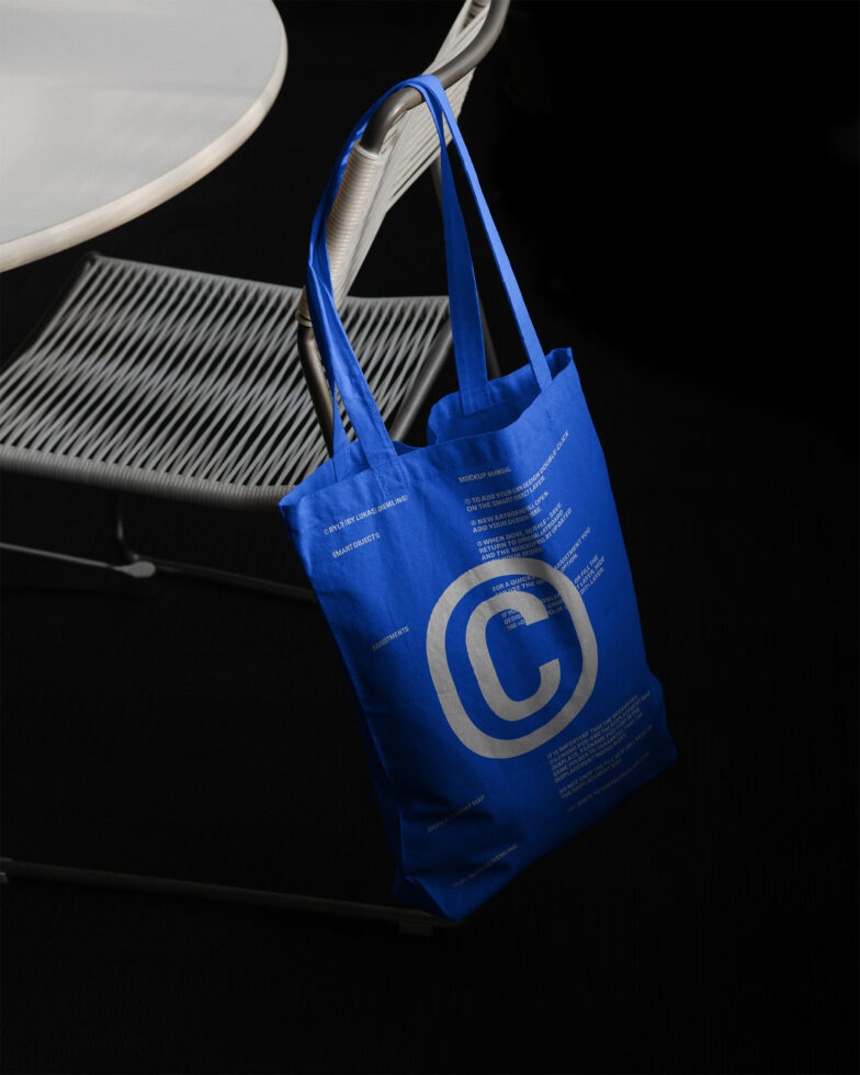 Blue tote bag hanging on a chair near a white round table Mockup design template featuring bold text Simple product presentation for designers