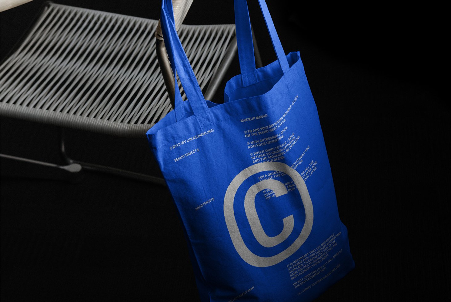 Blue tote bag mockup draped over a chair showcasing design instructions. Ideal for designers seeking customizable templates and smart objects for projects.