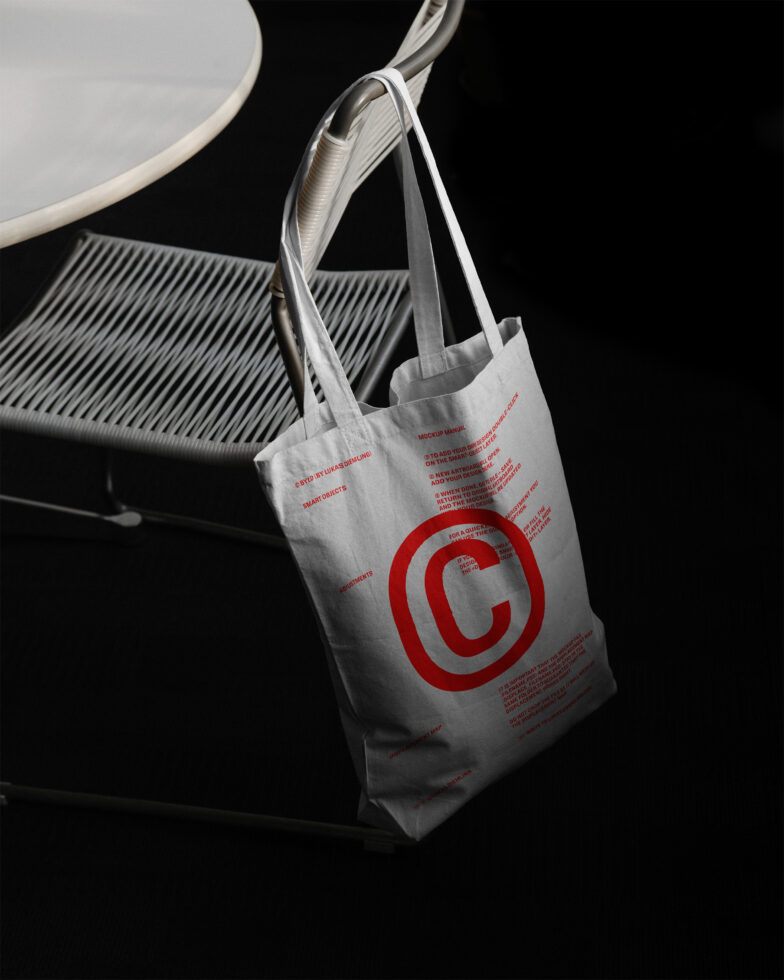 Tote bag mockup with red graphic on a white surface hanging on a white chair design asset for branding and presentation ideal for designers and creatives.