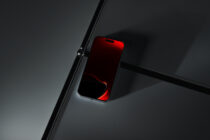 Red smartphone with glowing screen mounted on black metal rod against gray background