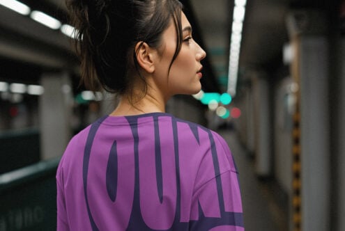 Woman wearing a purple graphic tee in an urban subway setting suitable for mockup templates. Ideal for designers working with apparel and streetwear design.