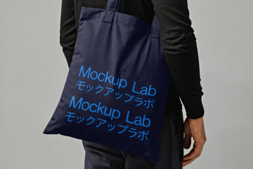 Tote bag mockup featuring blue text design on a black background held by a person in black clothing perfect for showcasing branding designs.
