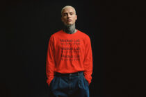 Person wearing bright red long-sleeve crewneck with small black repeated text, styled with blue denim