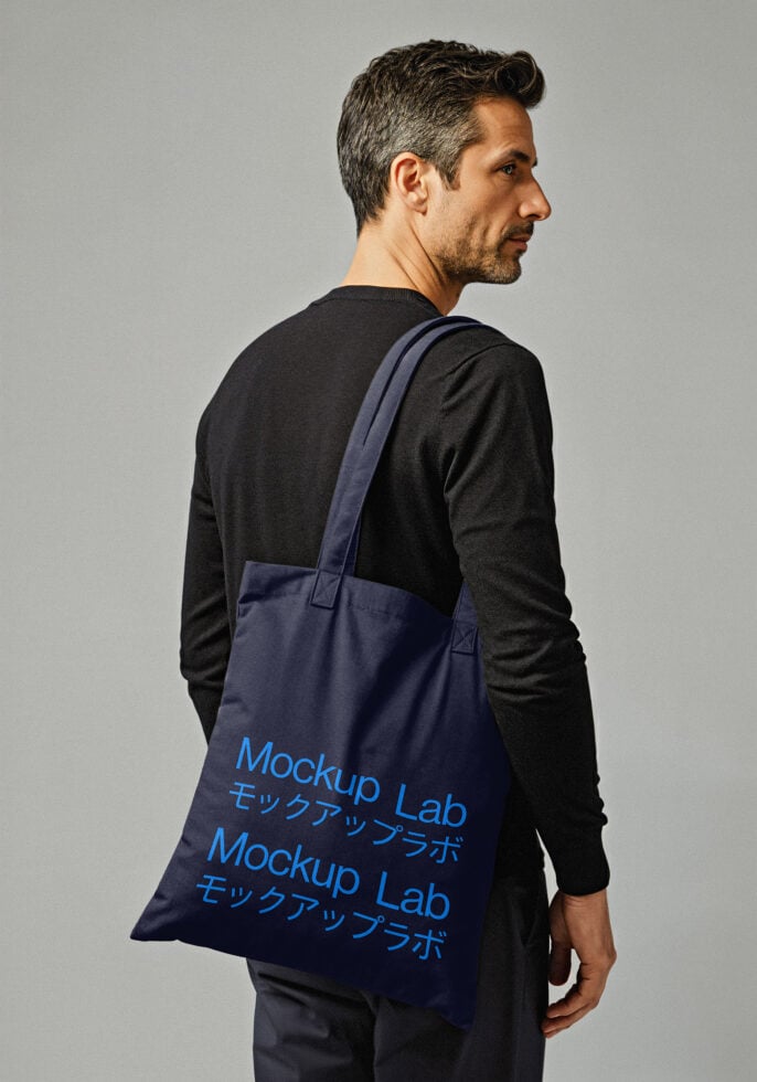 Man holding a tote bag mockup featuring blue typography suitable for design templates fashion accessories product presentation for graphic designers.
