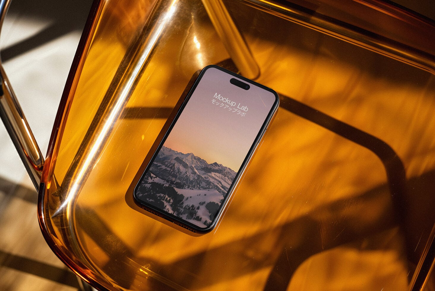 Mobile phone showing mountain landscape on amber glass surface with dramatic shadows