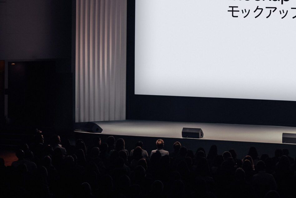 Large conference stage with a white screen and audience, suitable for event mockups, presentation graphics, or venue templates. Dark ambiance.