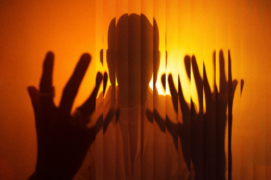 Silhouette of a person with hands on blinds, warm orange tones, perfect for designers seeking dramatic mood lighting, abstract graphic design resources.