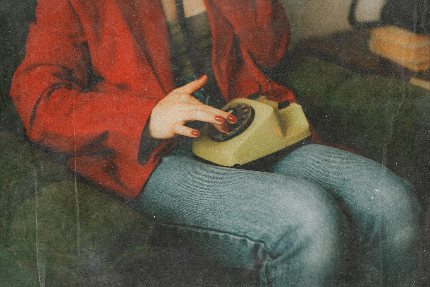 Vintage photo of a person in red jacket dialing a retro rotary telephone while sitting on a sofa. Perfect for retro-themed graphics or mockups.