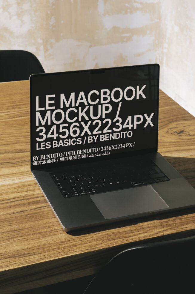 MacBook Pro mockup on wooden table with dark screen showing multilingual design typography