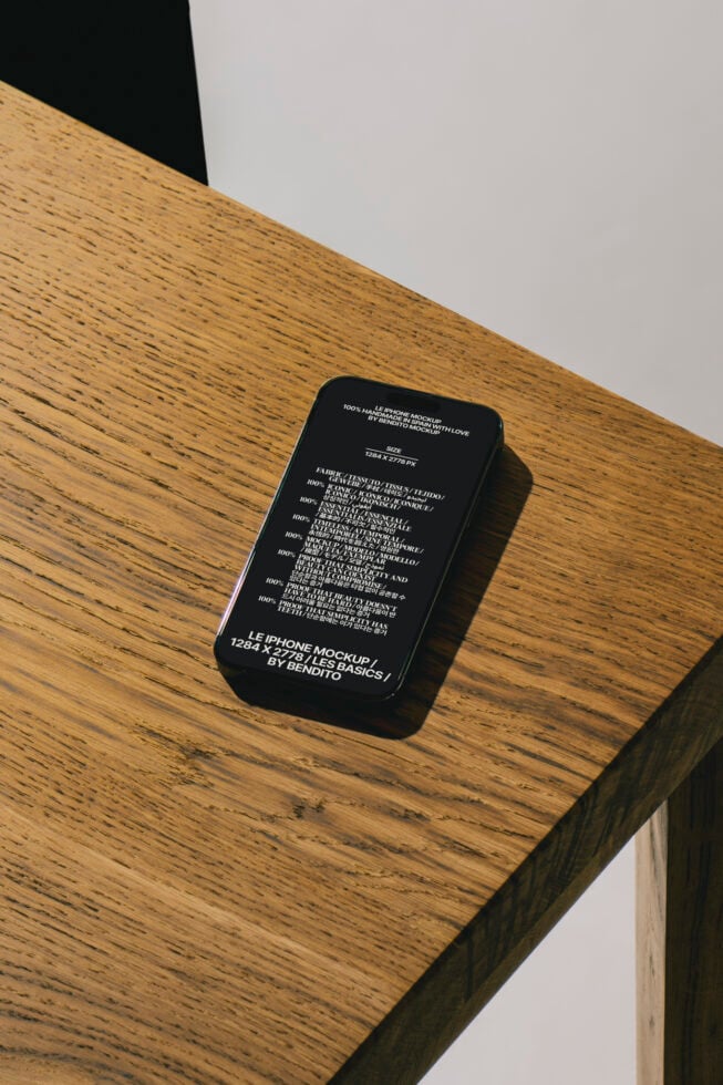 iPhone mockup placed on wooden desk surface perfect for design presentations. High-resolution graphic template for designers showcasing screen layouts.