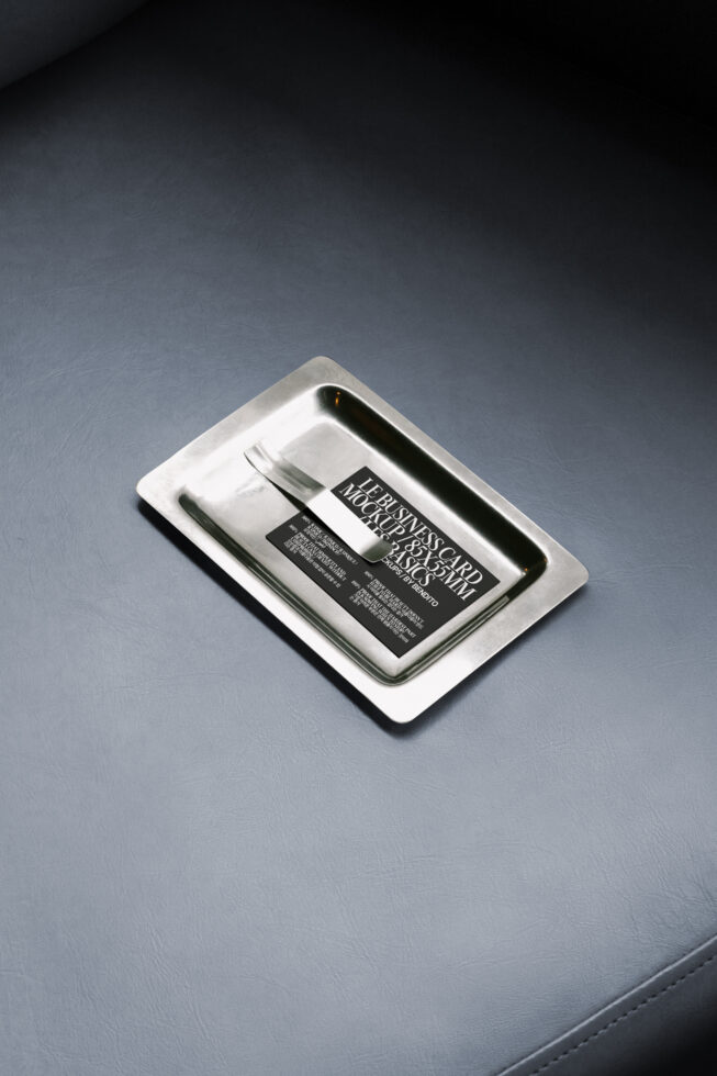 Business card mockup on a silver tray placed on a dark leather surface. Ideal for designers. Keywords: mockup, business card, graphic design.