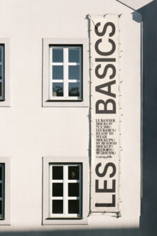 Tall vertical cream banner hanging on white building facade next to windows