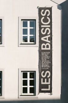 Tall vertical dark banner hanging on white building facade next to windows