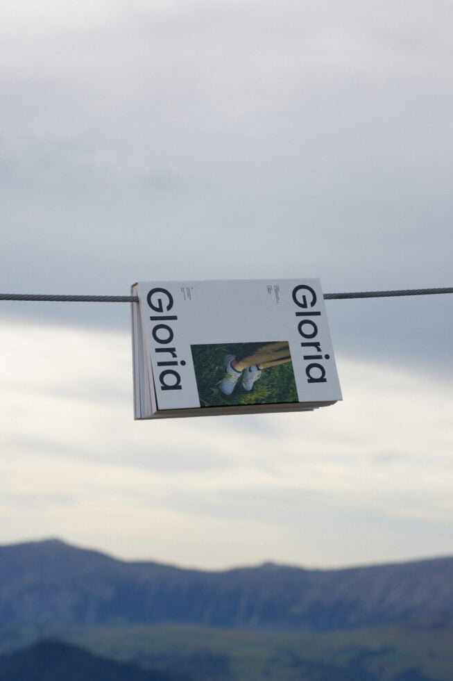 Magazine mockup featuring the word Gloria displayed on a wire with a scenic mountain background. Ideal for showcasing print designs. Keywords: Mockup, Magazine.