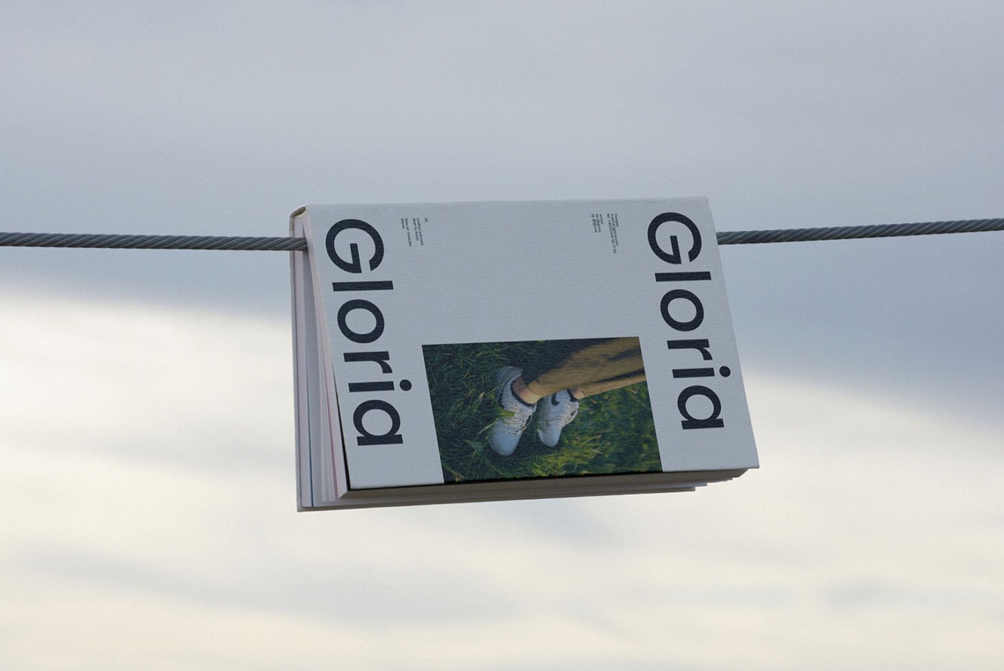 Magazine mockup featuring a minimalist design titled Gloria hanging on a cable. Ideal for showcasing print layout, typography, and branding concepts.