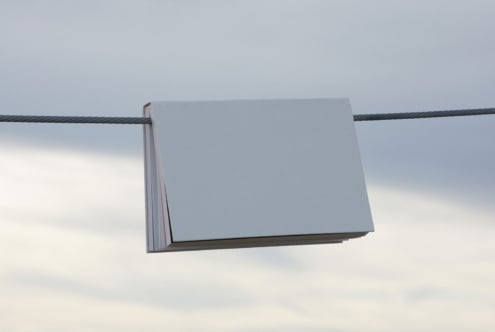 Minimalistic landscape mockup featuring a blank book hanging on a wire against a cloudy sky. Ideal for showcasing book covers and design projects.