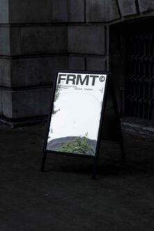 Outdoor sign mockup with urban backdrop featuring FRMT branding, reflecting buildings and foliage. Ideal for graphic designers and presentation templates.