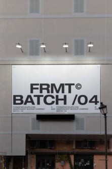 Building facade with large banner mockup displaying text FRMT BATCH 04. Ideal for showcasing outdoor advertisement designs. Urban setting with street lights.