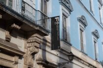 Black vertical banner on classical facade with carved stone columns, blue sky