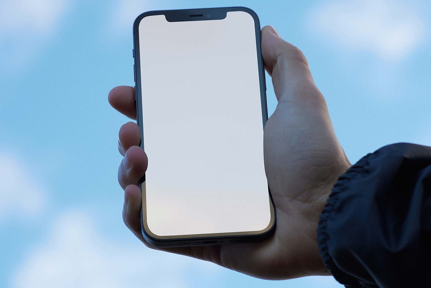 Blank iPhone screen held up outdoors against blue sky in natural light