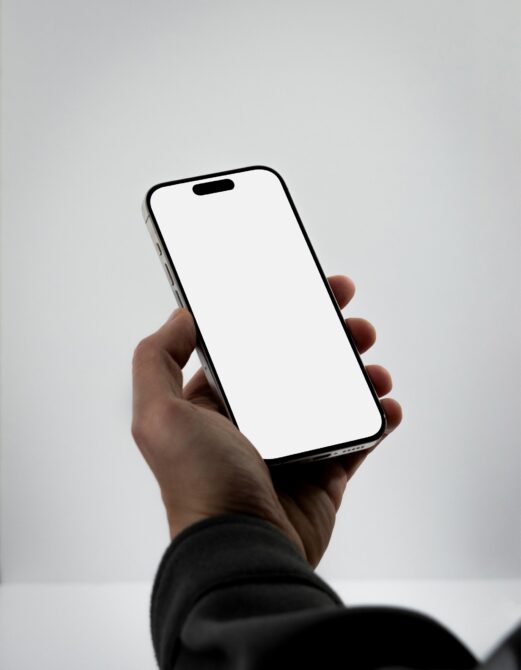Hand holding black phone with blank white screen on neutral light background