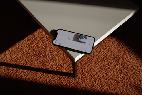 Smartphone mockup on a minimalist table corner with carpet texture. Ideal for showcasing mobile UI designs. Keywords: mockup, design, smartphone, UI.