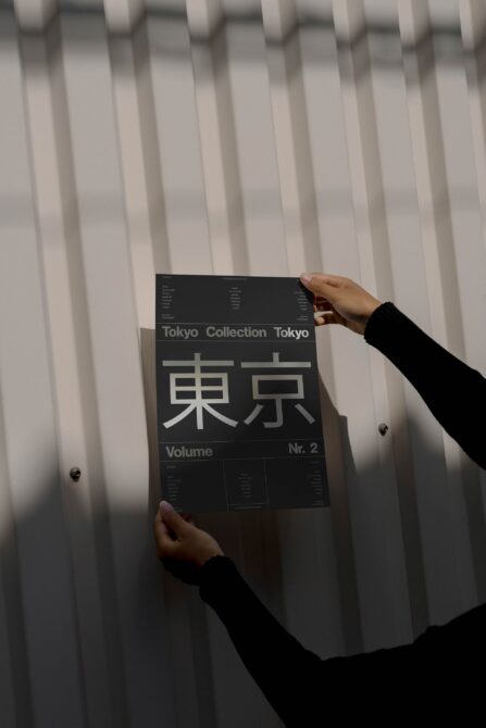 Designer holding a Japanese typography poster against a textured wall showcasing Tokyo Collection Volume Nr 2 modern graphic design mockup perfect for creatives.