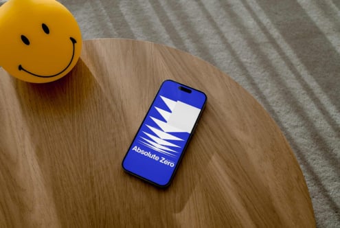 Smartphone mockup on wooden table displaying Abstract design with Absolute Zero text Bright smiley face object beside for creative designers templates