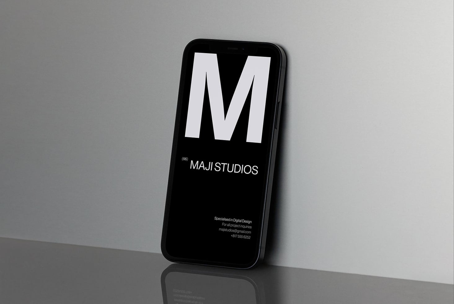 Black iPhone displaying Maji Studios portfolio homepage with large M logo on dark