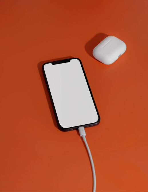iPhone with USB cable connected next to white earbuds on orange background